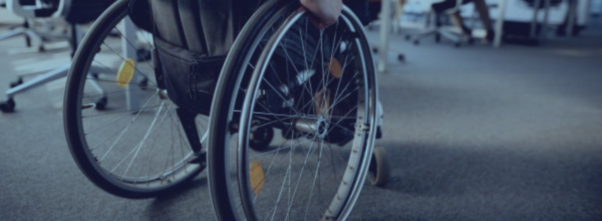 Plano detalle desde atrás de un empleado en silla de ruedas en una oficina moderna, simbolizando la integración laboral y la necesidad de ajustes razonables en la empresa tras una incapacidad permanente.