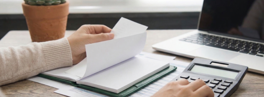 Persona revisando documentos contables con calculadora y ordenador portátil, representando el análisis de costes laborales y bases de cotización para 2026.