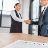 close-up view of contract on table and business people shaking hands behind