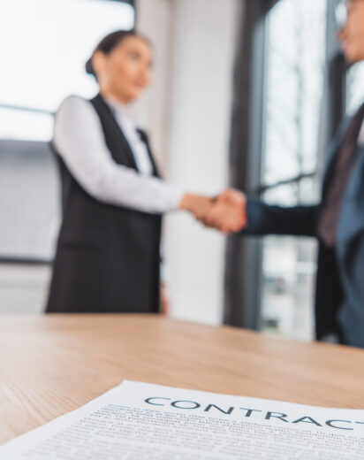 close-up view of contract on table and business people shaking hands behind