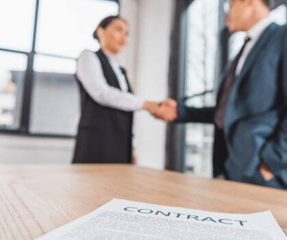 close-up view of contract on table and business people shaking hands behind