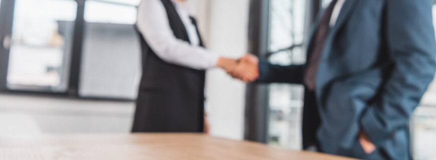 close-up view of contract on table and business people shaking hands behind
