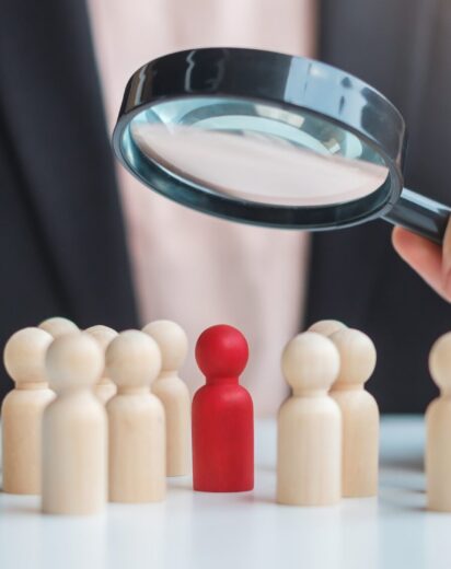Businesswoman hand holding magnifying glass for recruiting leader man wooden from crowd of employees.Human resource management, Recruitment, Teamwork, hiring and leadership Concepts