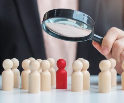 Businesswoman hand holding magnifying glass for recruiting leader man wooden from crowd of employees.Human resource management, Recruitment, Teamwork, hiring and leadership Concepts